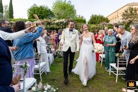 A happy couple happily walks among guests at the conclusion of their wedding ceremony at Santa Venerina - i Giardini di Villa Fago, as captured in this picturesque venue setting.